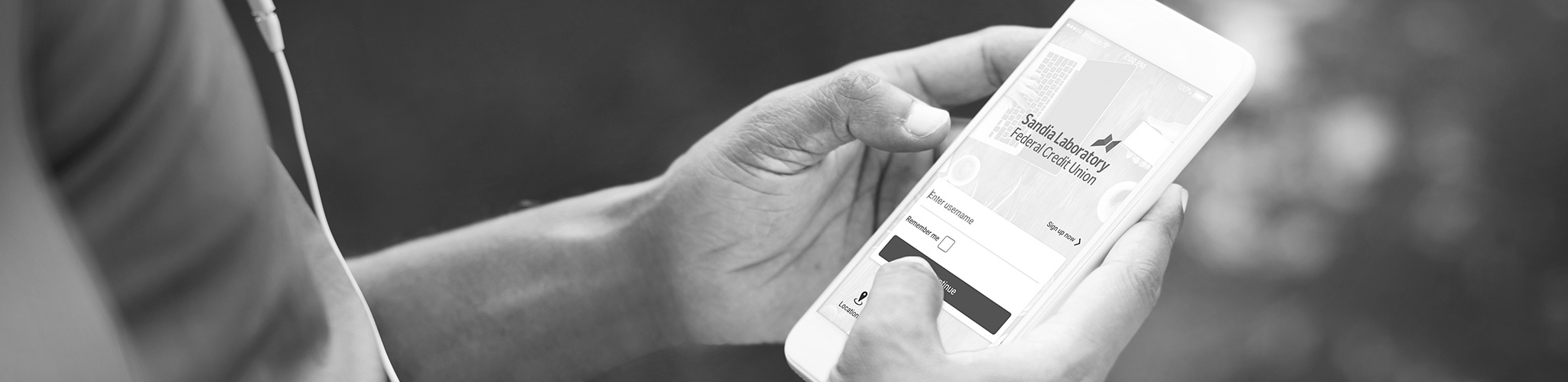 Male hands holding a phone showing a screenshot of SLFCU's new online banking system.