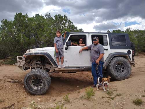 Woman, man, and son posing by their white Jeep with a dod