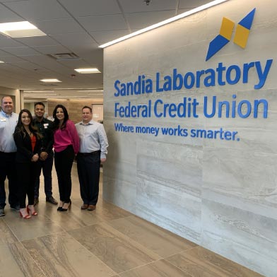 Jefferson employees standing next to SLFCU sign that reads: Sandia Laboratory Federal Credit Union. Where money works smarter."