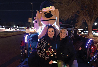 SLFCU Employees and Sandy the Lab pose in the back of a decorated truck for the Christmas Electric Light Parade