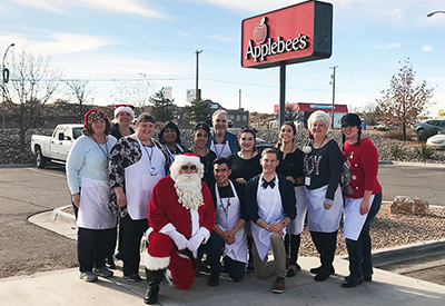 SLFCU employees pose with Santa Claus in front of the Applebee's sign in Los Lunas