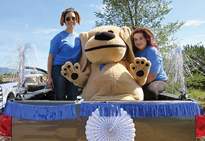 SLFCU Employees and Sandy the Lab pose in the back of a decorated truck for the Run, Rally and Rock Parade